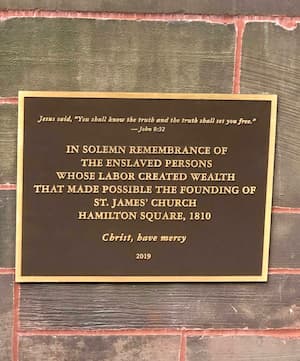 Plaque on a wall reading: "Jesus said, 'You shall know the truth and the truth shall set you free.' - John 8:32 IN SOLEMN REMEMBRANCE OF THE ENSLAVED PERSONS WHOSE LABOR CREATED WEALTH THAT MADE POSSIBLE THE FOUNDING OF ST. JAMES' CHURCH HAMILTON SQUARE, 1810 Christ, have mercy 2019"