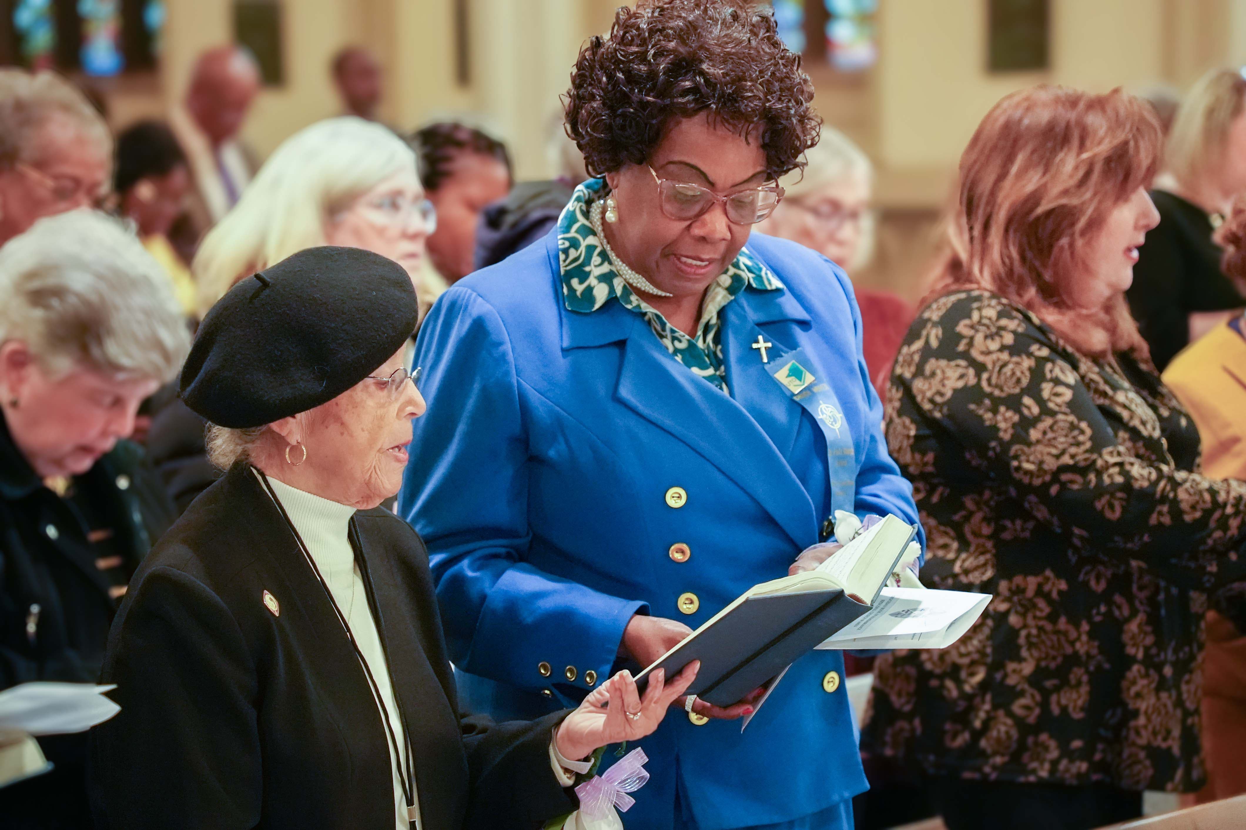 Two women saying a prayer out of a Book of Common Prayer