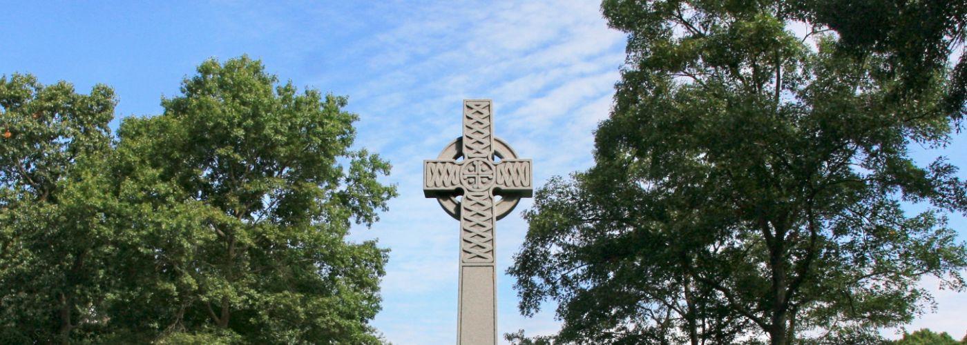 A large Celtic cross gravestone surrounded by trees