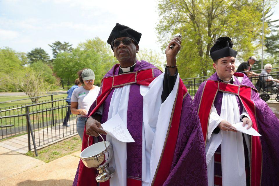 A priest wearing a biretta aspersing the Cathedral grounds