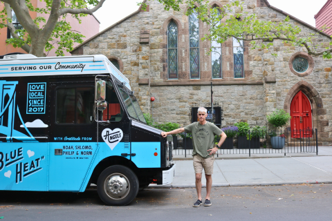 Fr. John Merz stands outside of a church next to the blue and black North Brooklyn Angels food truck